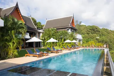 a pool at a resort with chairs and umbrellas at Villa Aye in Kamala Beach