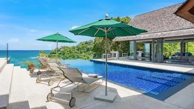a pool with chairs and umbrellas and the ocean at Villa Lomchoy in Phuket Town