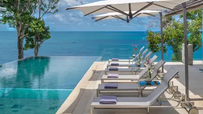 a pool with lounge chairs and the ocean at Villa Saengootsa in Phuket Town