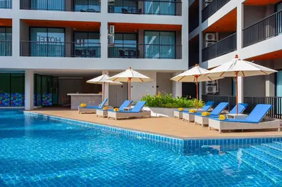 a swimming pool with chairs and umbrellas next to a building at 1 bed Corner apartment in Kata - Grand Kata VIP in Kata Beach