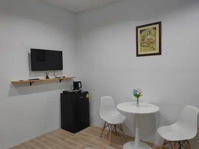 a room with a table and a tv and white chairs at Phudis Guest House in Ban Khlong Haeng