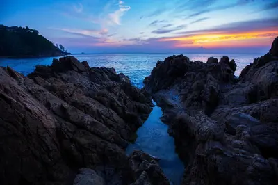 a sunset over the ocean with rocks and water at 2bdr Apartment Oceanstone Laguna by Capital Pro in Phuket Town