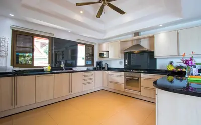 a large kitchen with wooden cabinets and a ceiling fan at Villa Malee , Sea View Infinity Pool, Staff, Chef in Kata Beach