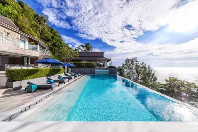an infinity pool with chairs and umbrellas next to a building at Villa La Prana in Phuket Town