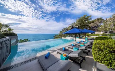 a pool with chairs and an umbrella and the ocean at Villa La Prana in Phuket Town