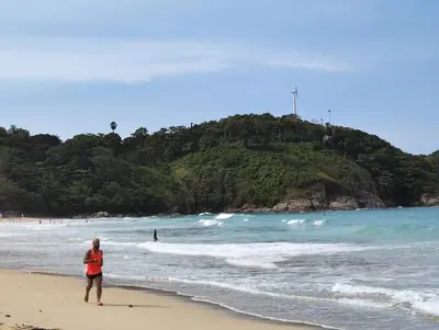 a man standing on a beach near the ocean at Nai Harn beach - Studio room on 2 floor at ReLife The Windy in Rawai Beach
