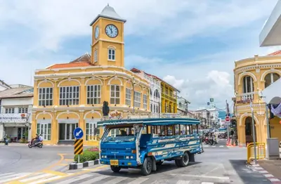 a blue bus driving down a city street with a clock tower at Private Pool Villa Nai Harn Beach in Rawai Beach