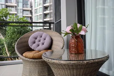 a rattan chair with a glass table and a vase with flowers at Cassia 1 BR Sea View apt by NLA in Bang Tao Beach