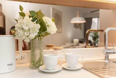 a vase of white flowers sitting on a counter with two cups at Cassia 1 BR Lake&Pool View apt by NLA in Bang Tao Beach