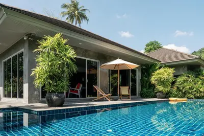 a swimming pool next to a house with an umbrella at VILLA FLORA - North Phuket, Naiyang Beach area in Nai Yang Beach