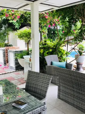 a patio with wicker chairs and tables and flowers at Guest House, shared pool, private bathroom and kitchen in Phuket Town