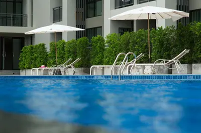 a swimming pool with chairs and umbrellas next to a building at Sugar Palm Residence in Phuket Town