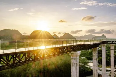 a bridge over a river with the sun setting over mountains at Beyond Skywalk Nangshi in Ban Met Nang Chi