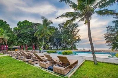 a row of lounge chairs next to a swimming pool with palm trees at Estella Phuket Mai Khao Beach Resort in Mai Khao Beach