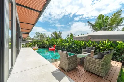 a patio with chairs and an umbrella and a swimming pool at New 3BR Pool Villa Long One A5 with Chalong Bay view in Chalong