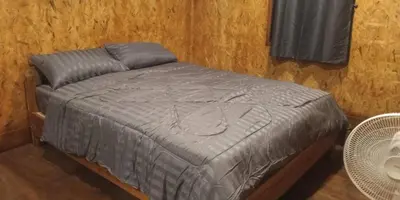 a bed with a gray comforter in a room at Sukanyawoodhouse in Ban Tha Rua