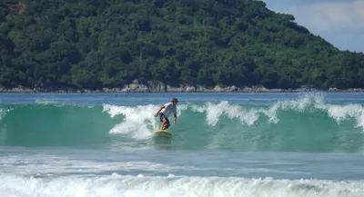a man riding a wave on a surfboard in the ocean at Coco Mountain View Guest House Hotel in Kata Beach