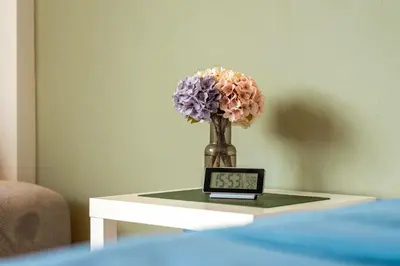 a vase of flowers sitting on a table with a clock at Ellie House Phuket Old Town in Ban Rangeng