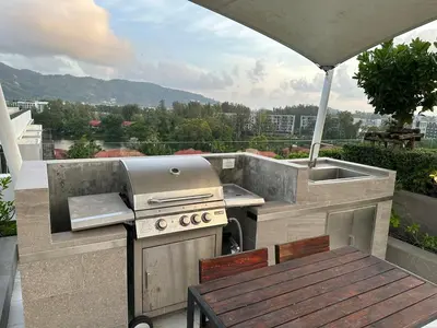 a outdoor kitchen with a grill and a table on a balcony at Laguna Skypark, 2 bedrooms & large terrace with golf view in Phuket Town