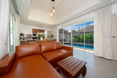 a living room with a brown leather couch and a kitchen at Bangtao villa 3 bedroom in Phuket Town