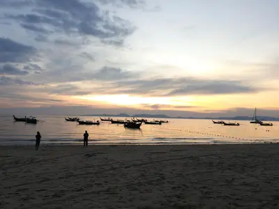 two people standing on a beach with boats in the water at Hello Montri in Klong Muang Beach