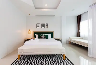 a white bedroom with a white bed and a black and white rug at Buasri Boutique Patong in Patong Beach