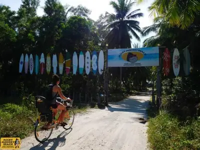 a man riding a bike down a road with surfboards at Micky Monkey Beach Hotel Phuket Maikhao Thailand in Mai Khao Beach