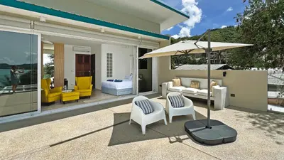 a patio with chairs and a table and an umbrella at At the Beach Spacious 2-level Design Home for 2-5 and 1 infant, Ao Yon Beach Phuket in Ban Ao Makham
