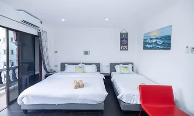 two beds in a room with a red chair at Belle Cose Guest House Phuket in Patong Beach