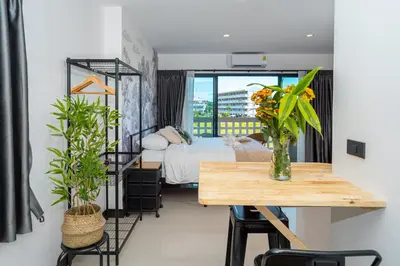 a room with a bed and a table and a bed and a window at Mitsu Guesthouse in Karon Beach