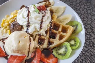 a white plate with waffles and ice cream and fruit at The Capuchin Hotel Krabi, Ao Nang Beach in Ao Nang Beach