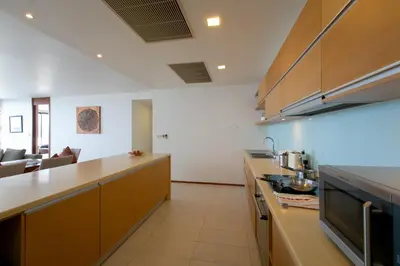 a kitchen with brown cabinets and a living room at Panoramic Sea View Luxury Apartment - Leelawadee21 in Kata Beach