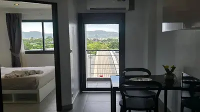 a bedroom with a bed and a table and a view of a balcony at Tranquil Tide 1 BR T1-605 in Chalong
