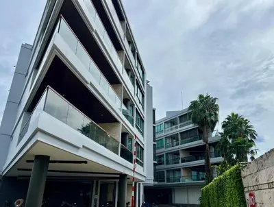 a white building with a palm tree in front of it at The Regent Bangtao by RESAVA in Bang Tao Beach