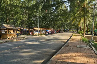 a street with a tree lined road with people walking down it at Mai Khao Beach Condo by Capital Pro in Mai Khao Beach
