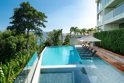 a swimming pool with chairs and an umbrella next to a building at Sea View 3BR Duplex in The Sapphire Bay 88 Residence near Patong and Paradise Beach in Patong Beach