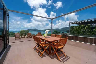 a wooden table and chairs on the deck of a house at Ocean Bliss - Sapphire Bay 3BR Apartment 812 with Terrace and Awe-Inspiring Views of Patong Bay in Patong Beach