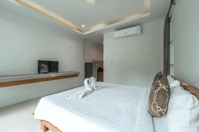 a bedroom with a bed with white sheets and a tv at Little Kamala Hill in Kamala Beach