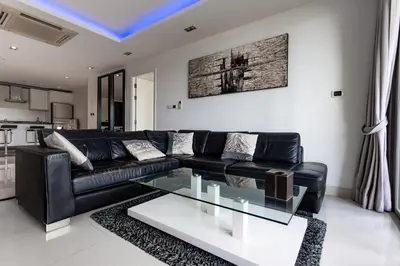 a living room with a black leather couch and a glass table at Nakalay Palm by Thaire in Kamala Beach