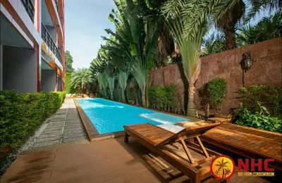 a swimming pool with a wooden bench next to a building at Nai Harn Condominium in Rawai Beach