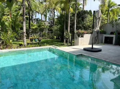 a blue swimming pool with an umbrella and trees at A lovely 2-3 bed only 300m walk to Bangtao Beach in Phuket