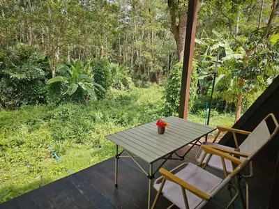 a table and chairs on a porch with a view of a forest at Cheewatra Farmstay Phuket ชีวาตรา ฟาร์มสเตย์ ภูเก็ต in Thalang