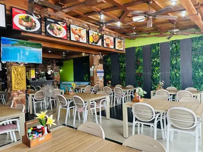 a restaurant with wooden tables and white chairs at Chang Hostel Patong Phuket in Patong Beach