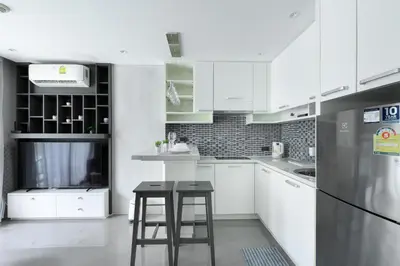 a white kitchen with two stools and a refrigerator at City Gate Kamala N103 by Phuket Sabay Rent in Kamala Beach