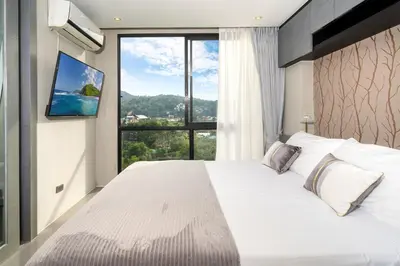 a bedroom with a large white bed with a large window at Citygate Kamala Resort in Kamala Beach
