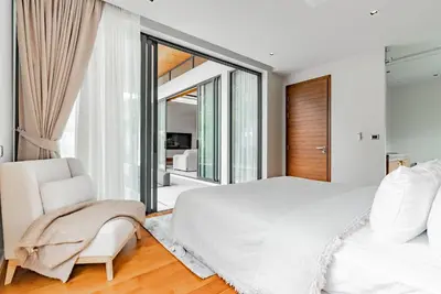 a white bedroom with a large bed and a chair at Botanica Modern Loft by Villacarte in Ban Pak Lak