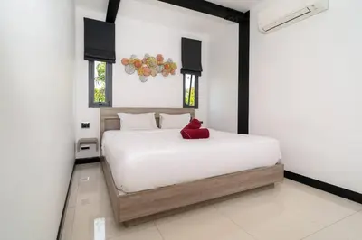 a bedroom with a white bed with a red pillow on it at New & Modern, Loft Style 4BR Villa Sunset Garden 3, 12m Salt Pool, just 10min drive Naiharn Beach in Rawai Beach
