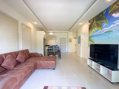 a living room with a brown couch and a large flat screen tv at Oasis 1 Bedroom Apartment In Rawai in Phuket Town