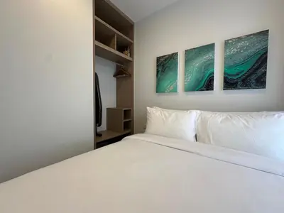 a white bed in a room with three paintings on the wall at 2 BD Skypark Condo with Terrace in Laguna Phuket