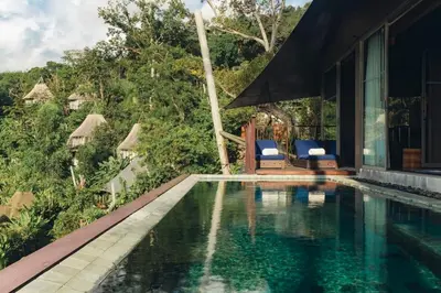 a swimming pool with two blue chairs next to a house at Keemala in Kamala Beach